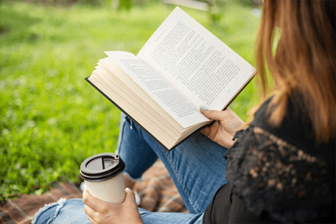 girl reading book and sitting outside, while holding a to-go coffee cup